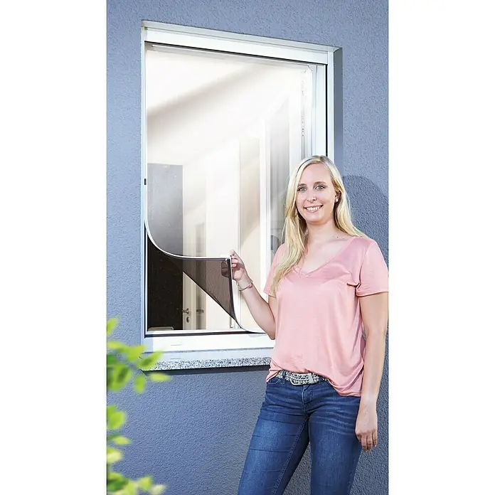Schellenberg Insect Stop Mosquitera Magnetic Reflection - An x Al: 100 x 120 cm, Color bastidor: Blanco, Montaje de la mosquitera: Fijación magnética - Mujer que muestra una mosquitera para ventanas. La mosquitera tiene un borde blanco y protege contra insectos.