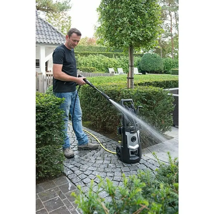 PowerPlus Hidrolimpiadora de alta presión POWXG90410 - 150 bar, 1.800 W, Capacidad de bombeo: 420 l/h - Un hombre está usando una hidrolimpiadora para limpiar un patio. La hidrolimpiadora es de color negro y plateado.