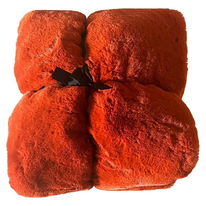 Decke LarissaPotters Clay, 180 x 140 cm, 100 % Polyester - Nahaufnahme einer leuchtend orangefarbenen, zusammengebundenen Kuscheldecke mit einer schwarzen Schleife auf schwarzem Hintergrund.