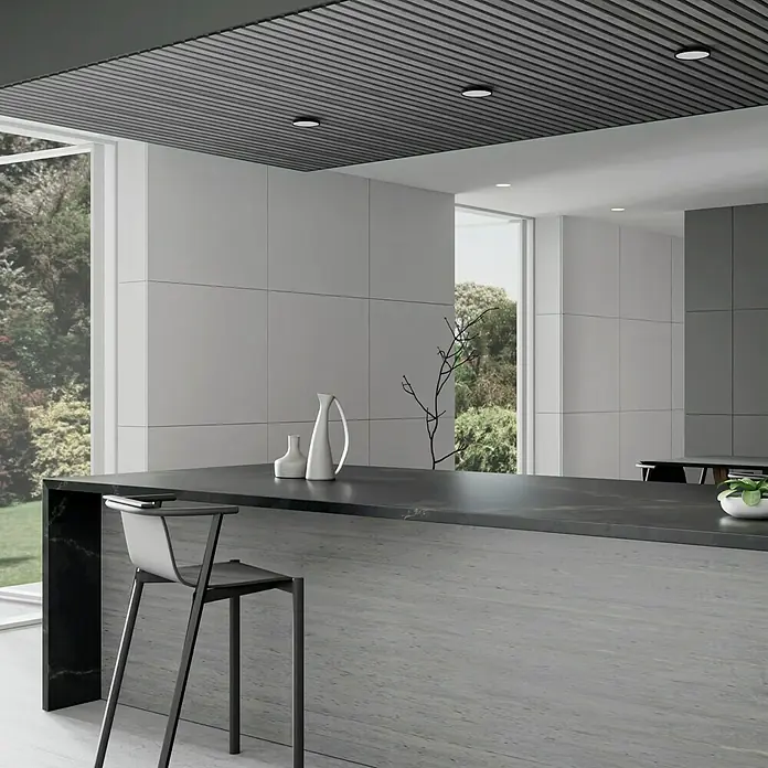 Panel acústico decorativo Premium Plus - 1,2 m x 0,6 m x 22 mm, Roble gris - Cocina moderna con una elegante isla negra y un taburete de bar elegante. El diseño minimalista destaca su elegancia.