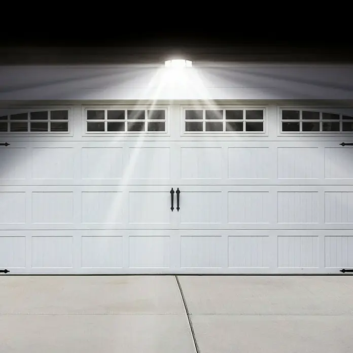 Proyector LED solar Beyong Bight X3 - Blanco frío, 1.000 lm - Primer plano de una puerta de garaje blanca con ventanas debajo de una lámpara de techo que emite un brillo.