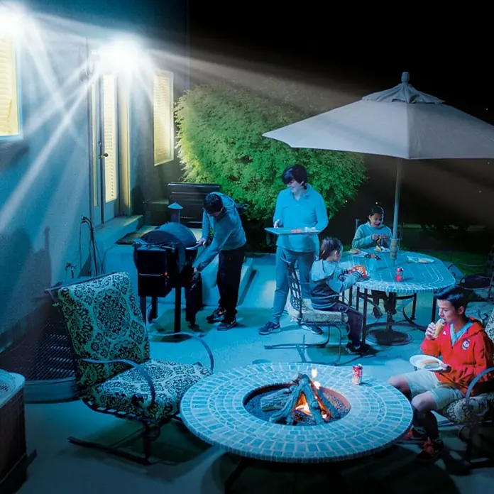 Proyector LED solar Beyong Bight X3 - Blanco frío, 1.000 lm - Una familia disfruta de una barbacoa en el jardín, con un brasero que proporciona calor y luz.