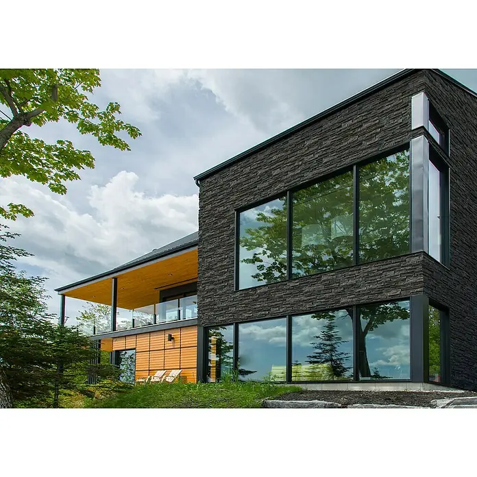 Stegu Verblendstein-Ecke Kongo - 37,5 cm x 12 cm x 16 mm, Graphit, Steinoptik - Moderne Hausfassade mit großen Fenstern und Steinverkleidung, die Architektur und Natur harmonisch verbindet.