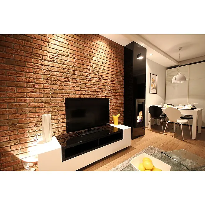 Stegu Verblendstein Country 640 - 20,5 x 6,2 cm, Braun/Rot, Steinoptik - Wohnzimmer mit TV-Möbeln in Weiß und Schwarz, die sich elegant in das moderne Interieur einfügen. Der warme Backsteinwandhintergrund ergänzt das Gesamtbild.