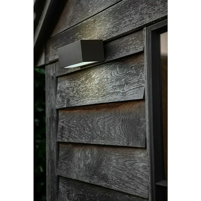 Lutec LED-Außenwandleuchte Gemini - 10,5 W, 14 x 9 x 6,5 cm, Anthrazit, IP54 - Moderne, rechteckige Außenleuchte aus dunklem Metall an einer rustikalen Holzwand, die einen hellen Lichtschein nach unten wirft.