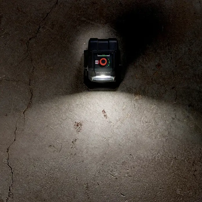 Metabo CAS 18V LED-Akkustrahler BSA 12-18 LED 2000 - 18 V, Ohne Akku, 2.000 lm - Metabo Akku-Baustrahler auf Betonboden, der den Bereich darunter beleuchtet. Ein vielseitiger und robuster Strahler für den Baueinsatz.