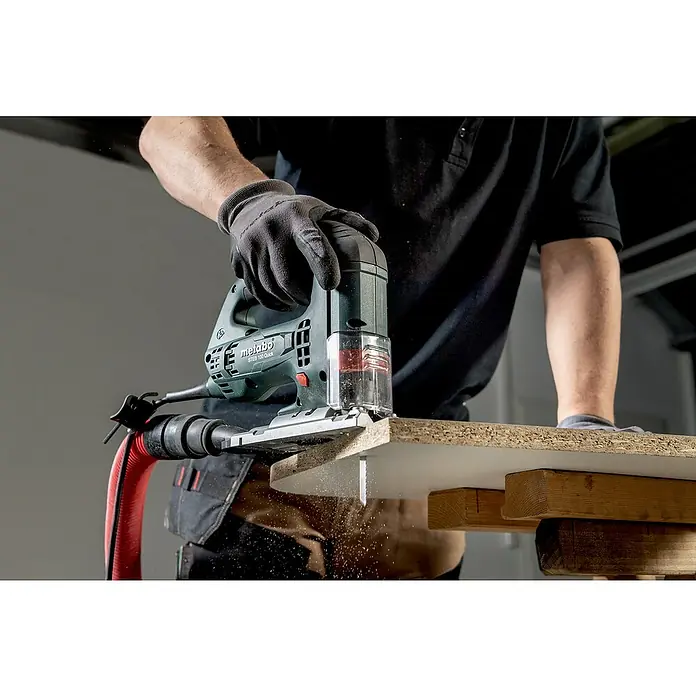 Metabo Elektro-Pendelhubstichsäge STEB 100 Quick - 1.000 /min - 3.100 /min, Max. Schnitttiefe in Holz: 100 mm, Anzahl Pendelhubstufen: 4 Stk. - Eine Metabo Stichsäge ST EDB 100 Quick sägt ein Stück Holz, während ein Arbeiter das Werkzeug mit Handschuhen bedient, um Staub zu entfernen.
