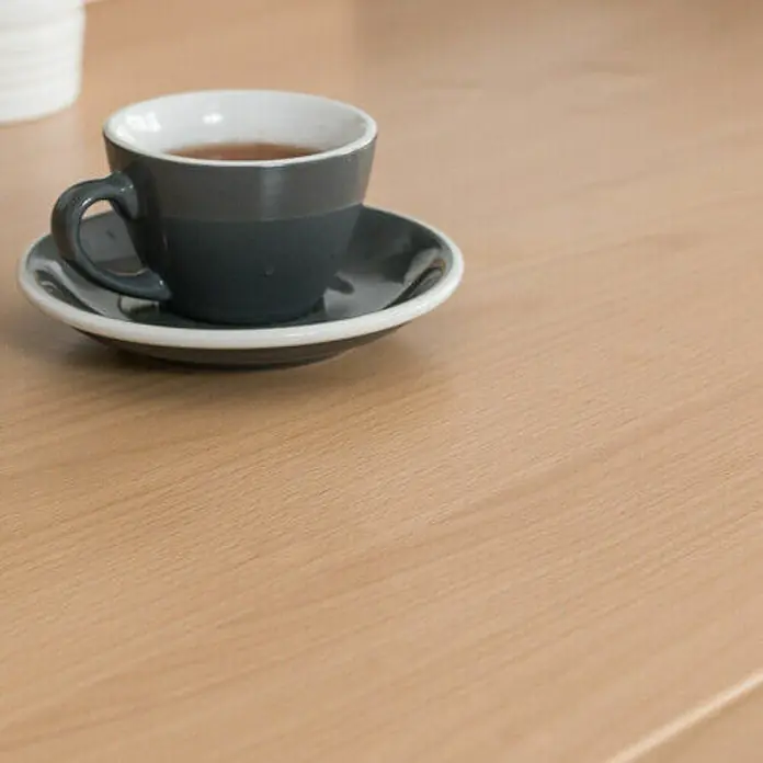 D-c-fix Lámina efecto madera - Haya, 210 x 90 cm, Madera de haya, Autoadhesivo - Primer plano de una taza de café gris y un plato sobre una mesa de madera, perfecto para una pausa de café acogedora.
