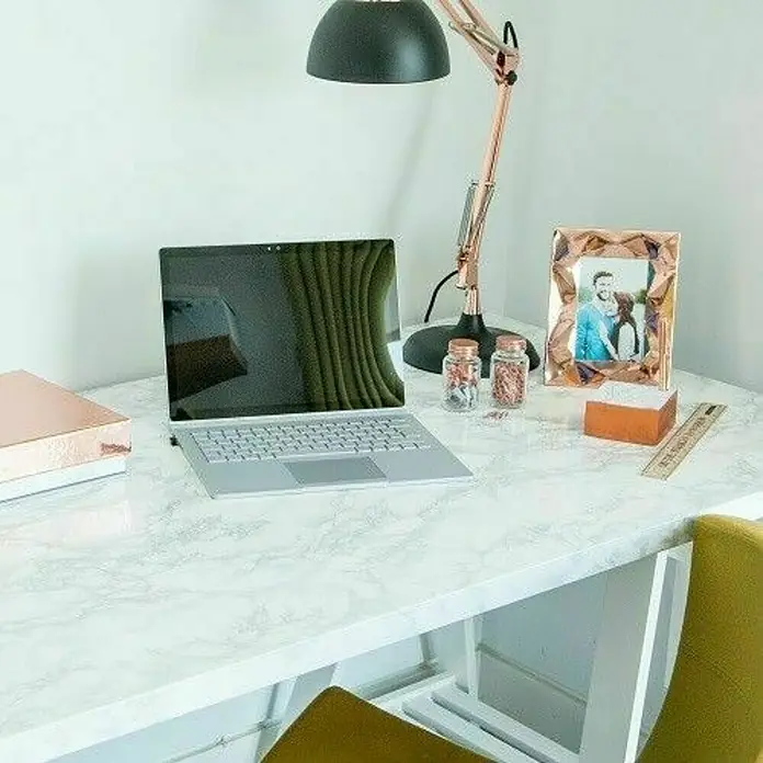 D-c-fix Lámina adhesiva efecto mármol blanco - An x L: 45 x 200 cm - La foto muestra un escritorio con un portátil, una lámpara y objetos decorativos, creando un espacio de trabajo moderno y elegante.