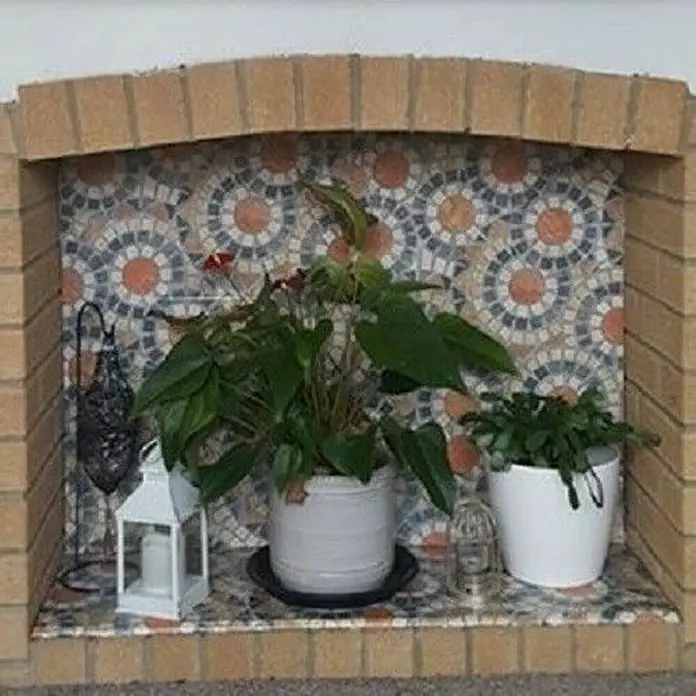 D-c-fix Lámina adhesiva efecto piedra pianetra - An x L: 45 x 200 cm - Primer plano de una chimenea decorativa con ladrillos, azulejos de mosaico y plantas en macetas, creando un ambiente cálido y acogedor.