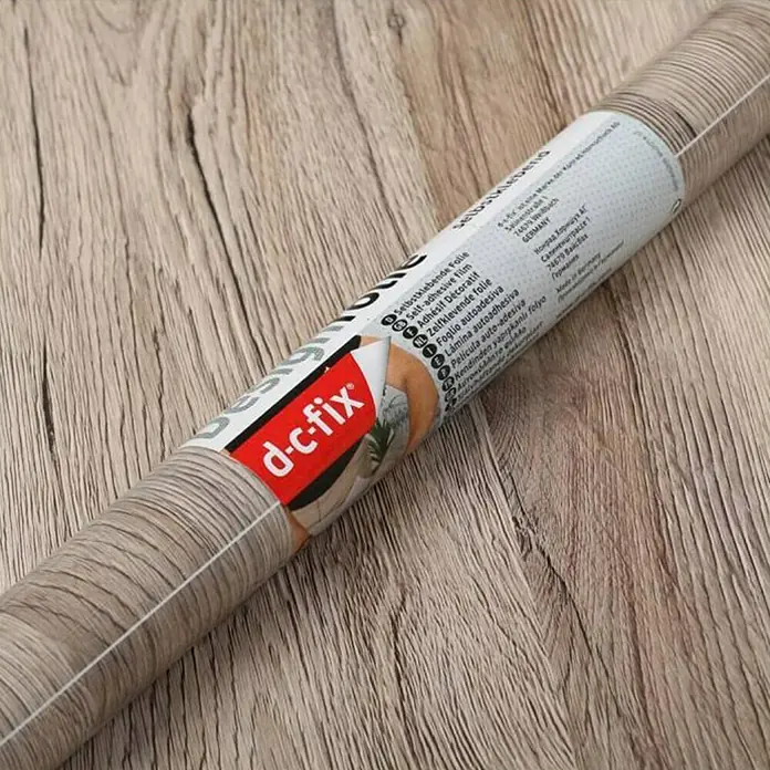 D-c-fix Lámina para ventana efecto madera sanremo - 45 x 200 cm - Primer plano de un rollo de lámina autoadhesiva d-c-fix con diseño de veta de madera. Ideal para renovar muebles.