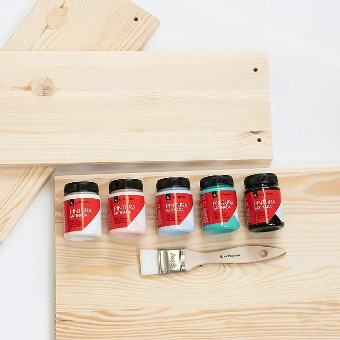 La Pajarita Pintura satinada - Carmín, 75 ml, Satinado - Foto del producto con botes de pintura La Pajarita y un pincel con tablas de madera. Ideal para proyectos de manualidades y DIY.