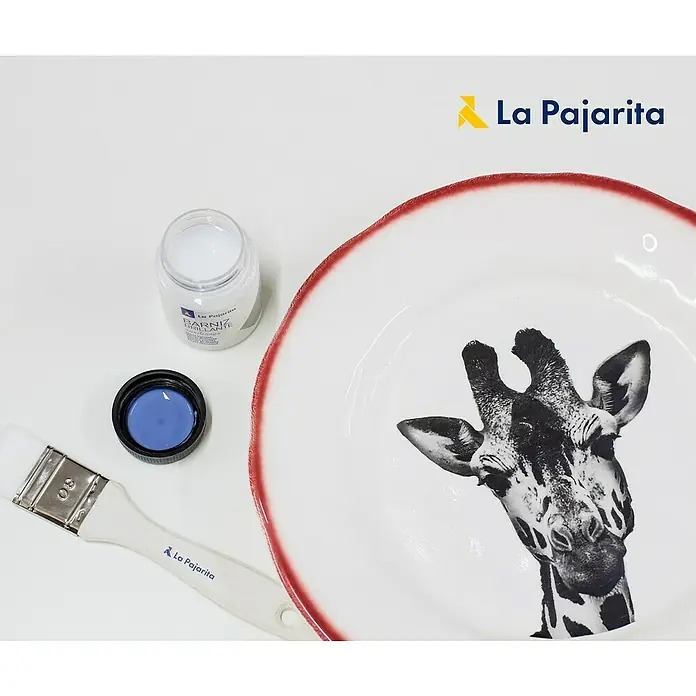 La Pajarita Barniz - incoloro, 175 ml, Mate - Primer plano de un plato con diseño de jirafa, un bote de barniz, un pincel y el logo de La Pajarita.