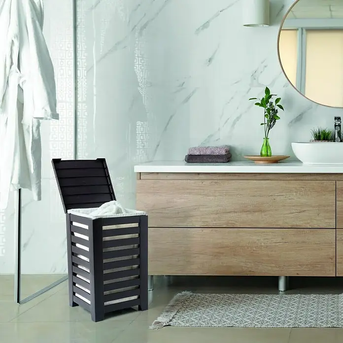 Tatay Cubo para la ropa Lombok Pongotodo - L x An x Al: 34 x 34 x 58 cm, Marrón - Un cesto para la ropa sucia abierto de madera oscura con listones en un baño, situado junto a un tocador moderno y un toallero.