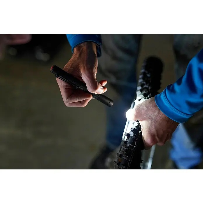 Ledlenser Taschenlampe P4 Core - 15 lm - 120 lm, IP54 - Nahaufnahme einer Person, die mit einer Stablampe einen Fahrradreifen untersucht, wobei der Fokus auf der praktischen und präzisen Beleuchtung liegt.