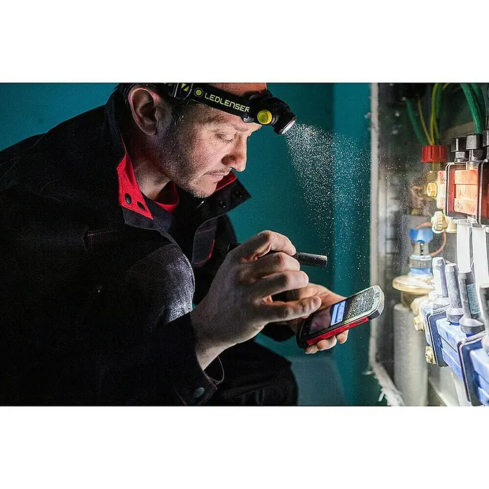 Ledlenser Taschenlampe P2R Work - 110 lm - Nahaufnahme eines Mannes, der eine LEDLENSER Stirnlampe trägt und ein Smartphone in der Hand hält. Ideal für Handwerker.