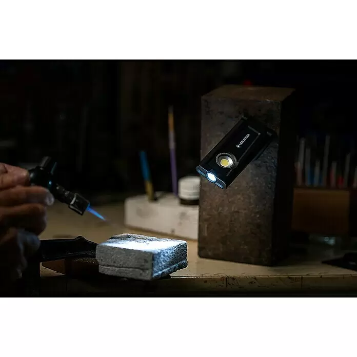 Ledlenser LED-Arbeitsleuchte iF2R - 200 lm, IP54 - Schwarze Ledlenser Taschenlampe beleuchtet Werkbank, während eine Person einen Brenner benutzt. Kompaktes Arbeitslicht.