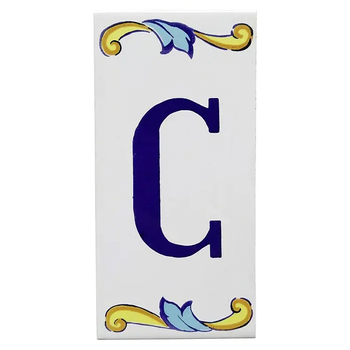 Pavimento cerámico Letra C - 7,5 x 15 cm, Blanco/Azul/Amarillo, Brillante - Baldosa decorativa con la letra C en azul, adornada con ornamentos amarillos y azules en la parte superior e inferior sobre un fondo blanco.
