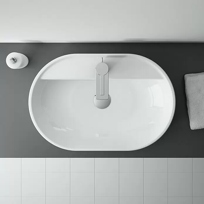 Inspira Aufsatzwaschbecken - 62 x 41 cm, Keramik, Weiß - Blick von oben auf ein weißes, ovales Keramik-Waschbecken mit Chromarmatur, Seifenspender und grauem Handtuch.