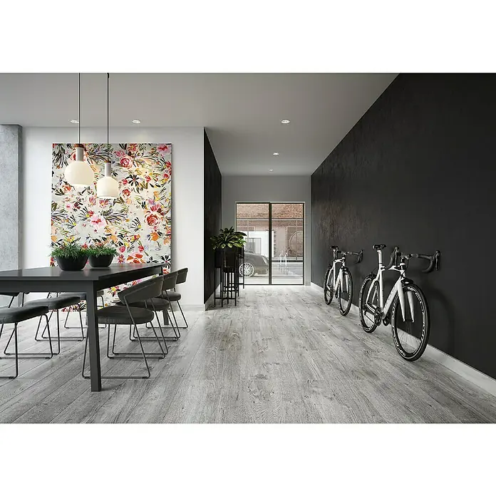 LOGOCLIC Laminado Roble Ferik - 1.380 x 193 x 10 mm, AC4 - Un interior moderno con una mesa de comedor oscura, sillas, cuadro floral colorido y dos bicicletas blancas contra la pared oscura.