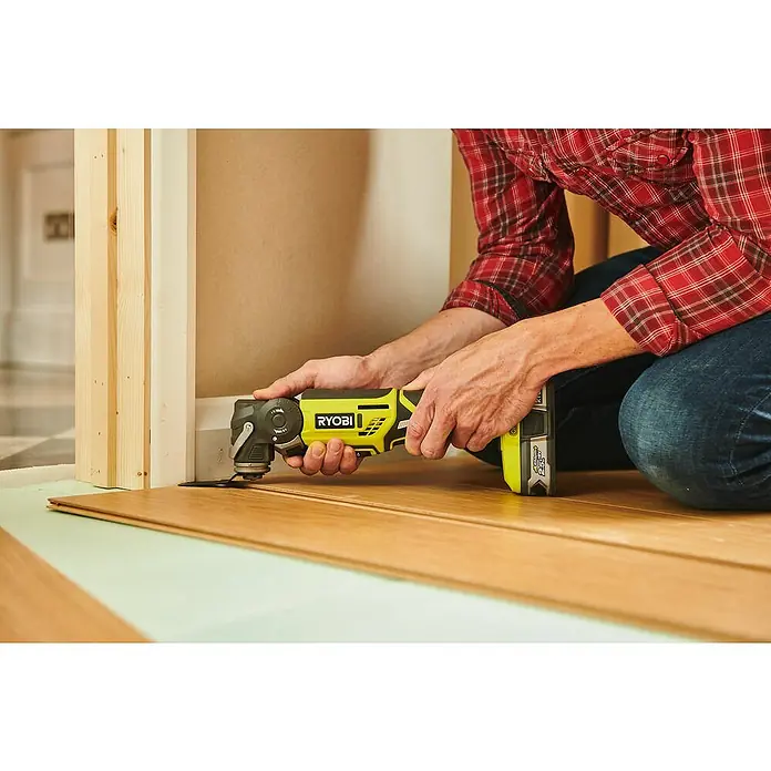 Ryobi ONE+ Akku-Multifunktionswerkzeug R18MT-0 - 18 V, Ohne Akku - Nahaufnahme eines Handwerkers, der mit einem gelben Ryobi Multifunktionswerkzeug einen Holzboden an einer Wand zuschneidet.