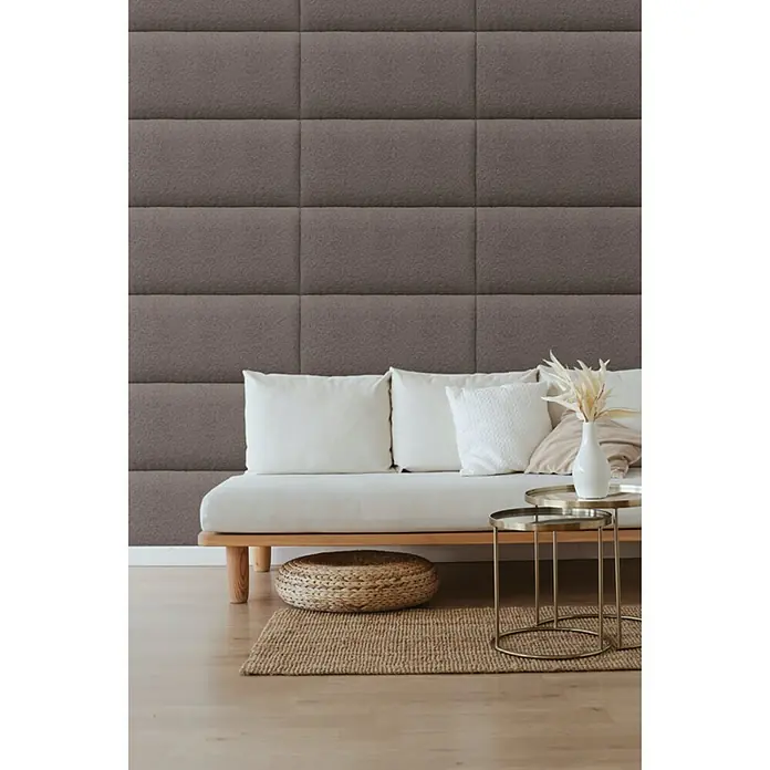 Fllow Wandpolster Wolke - Schoko, 60 x 30 cm - Das Bild zeigt eine moderne Inneneinrichtung mit braunen Wandpaneelen, einem hellen Sofa und einem runden Teppich, der eine gemütliche Atmosphäre schafft.