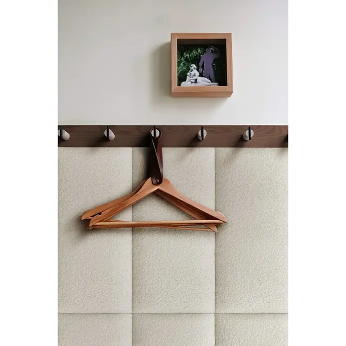 Fllow Wandpolster Wolke - Naturweiß, 60 x 30 cm - Nahaufnahme eines Holzkleiderbügels, der an einer Wand hängt, mit einem Kunstwerk darüber, das ein besonderes, modernes Ambiente erzeugt.
