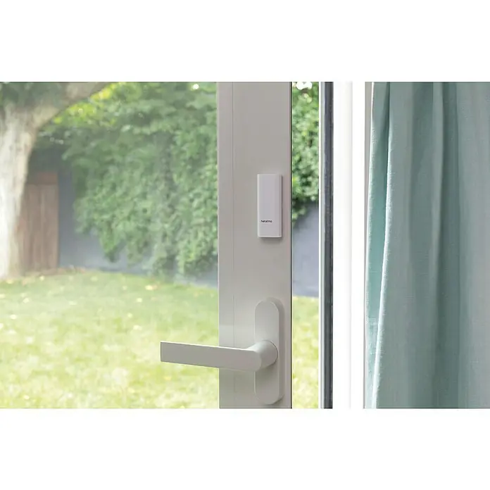 Netatmo Sensor de ventana y puerta inteligente - Específico para: Puertas y ventanas - Primer plano de un sensor de seguridad Netatmo conectado a un marco de ventana blanco, destacando la protección inteligente del hogar.