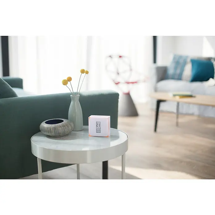 Netatmo Termostato inteligente - L x An x Al: 2,2 x 8,3 x 8,3 cm - Foto interior de un termostato de ambiente inteligente sobre una mesa, que regula la temperatura. El diseño moderno se integra bien en los espacios habitables.