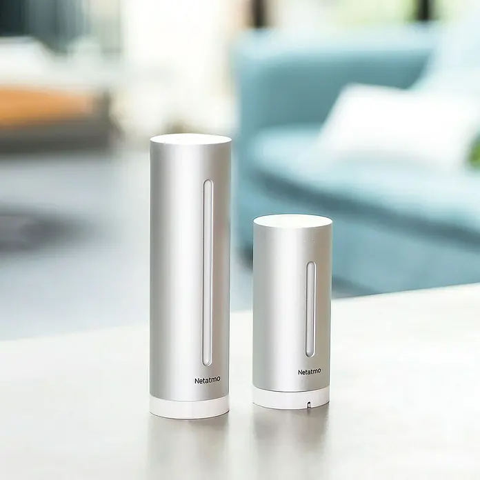 Netatmo Estación meteorológica inalámbrica - Plateado - Dos estaciones meteorológicas Netatmo plateadas sobre una mesa, una versión más grande y otra más pequeña, para datos precisos.