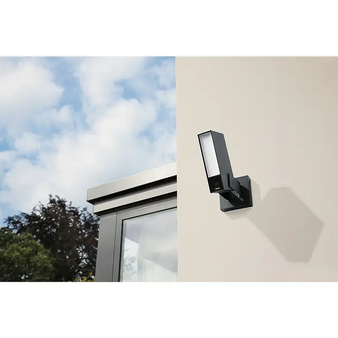 Netatmo Cámara de vigilancia Inteligente - Negro, Ángulo de detección: 100 °, Alcance de detección: 15 m - Imagen de una cámara de seguridad negra con foco conectado a una pared, que proporciona iluminación y vigilancia exterior segura.