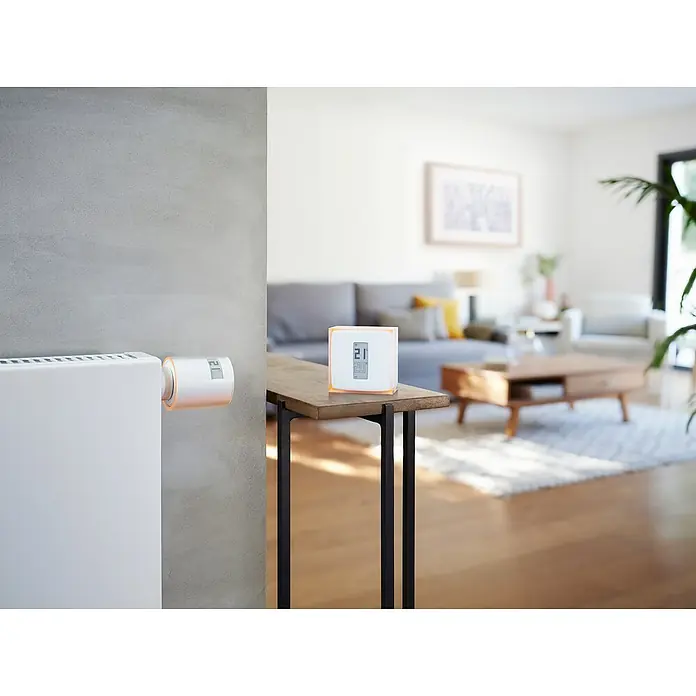 Netatmo Juego de termostato y válvulas - 3 válvulas Netatmo - Primer plano de un termostato de radiador inteligente y un termostato Smart Home en un salón.