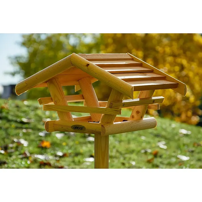 Dobar Vogelhaus Bernie Bernstein - 44 x 44 x 101 cm, Holz, Braun - Ein hölzernes Vogelhaus auf einem grünen Rasen mit Bäumen im Hintergrund. Das Vogelhaus hat ein schindelgedecktes Dach und ein rundes Podest.
