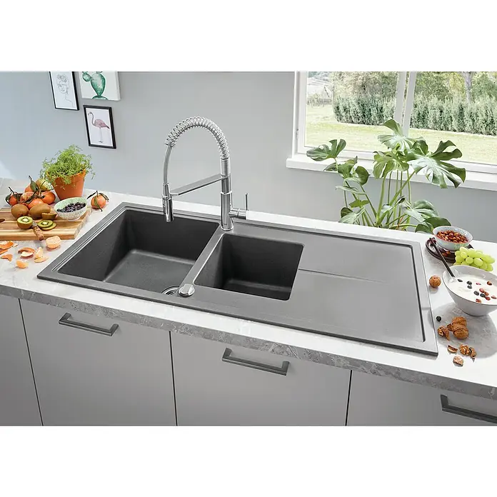 Grohe QuickFix Get Grifo de cocina profesional - Cromo, Brillante - Un fregadero de cocina con dos cubetas y un escurridor está colocado sobre una encimera, junto a fruta y una planta.