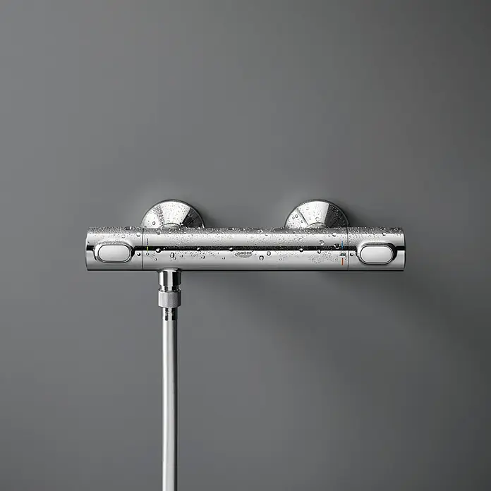 Grohe Brausethermostat Precision Flow - Chrom - Nahaufnahme eines glänzenden Grohe Duschthermostats mit Wassertropfen vor einem grauen Hintergrund.