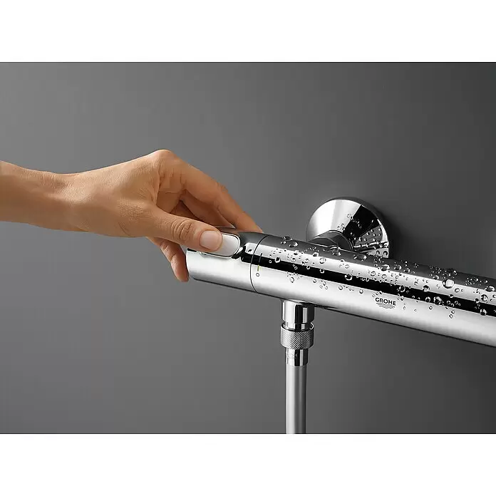 Grohe Brausethermostat Precision Flow - Chrom - Hand betätigt eine verchromte Duschthermostatstange mit Wassertropfen und angeschlossenem Schlauch.