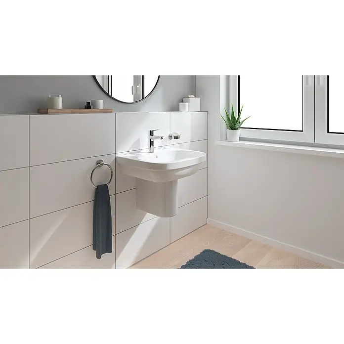 Grohe Start Grifo de lavabo M - Cromo, Resplandeciente, Barra de tracción - Un moderno lavabo de baño con grifo, jabonera y toallero está montado contra paredes de azulejos blancos. Una planta en la ventana.
