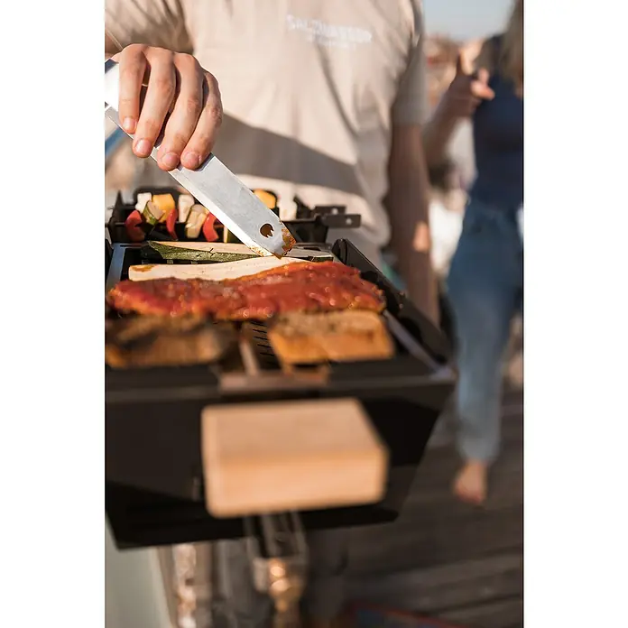 Knister Grillzange - Länge: 22 cm - Eine Person grillt Speisen auf einem tragbaren Grill, darunter Fleisch, Gemüse und Brot, mit Grillspießen.