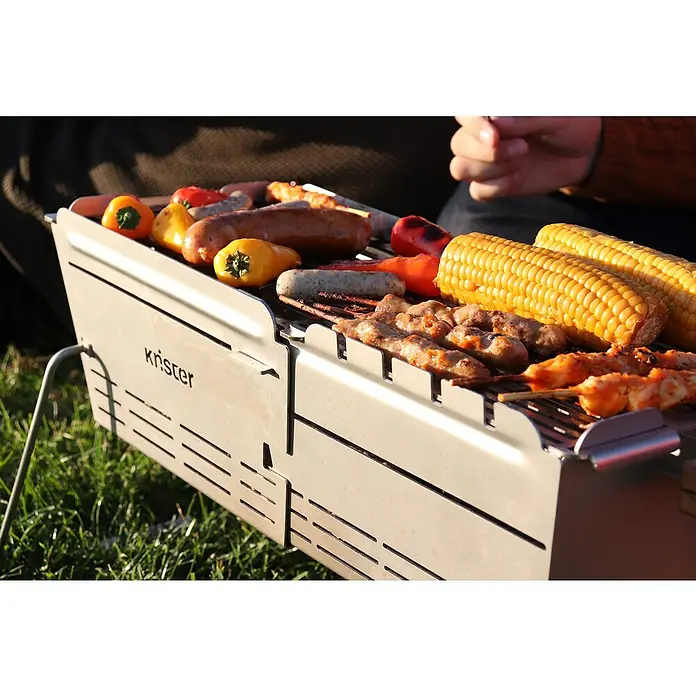Knister Holzkohlegrill Premium - Grillfläche (B x T): 52 x 22 cm, Silbergrau - Grill mit Würstchen, Paprika, Maiskolben und Spießen auf dem Grillrost. Der Grill ist von der Marke Krister.