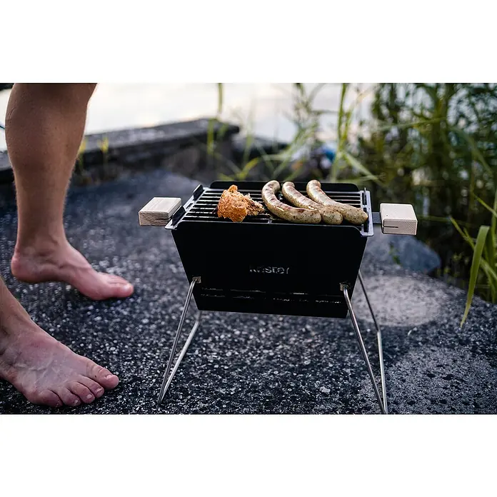 Knister Holzkohlegrill - Grillfläche (B x T): 28 x 20 cm, Schwarz - Nahaufnahme eines Kistér-Grills mit Würstchen und Brot, der eine gemütliche Outdoor-Kochatmosphäre schafft.