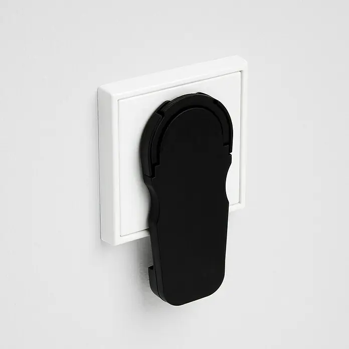 Voltomat Flachstecker - Schwarz - Schwarze Kindersicherung an einer weißen Steckdose, die das Risiko von Stromschlägen reduziert.