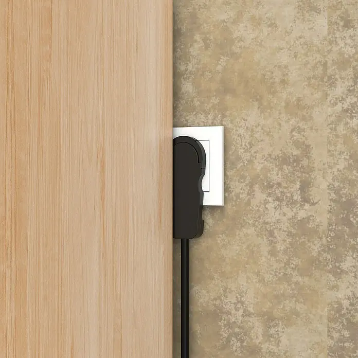 Voltomat Flachstecker - Schwarz - Steckdose mit eingestecktem schwarzem Stecker an einer beigen Wand neben einer Holztür.