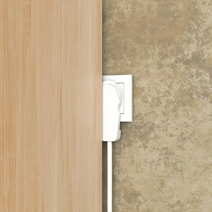 Voltomat Flachstecker - Weiß - Das Bild zeigt eine weiße Steckdosenabdeckung an einer Wand neben einem Türrahmen. Es schützt vor versehentlichem Kontakt mit der Steckdose.