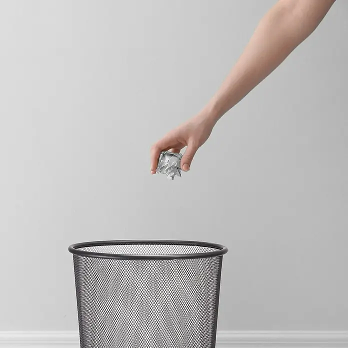 Zeller Present Papierkorb Mesh - Ø x H: 26 x 28 cm, Metall, Anthrazit - Ein zerknülltes Papier wird in einen schwarzen Metallmülleimer geworfen, der vor einer schlichten weißen Wand steht.