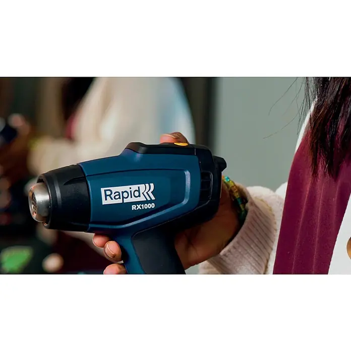 Rapid Power for All 18V Akku-Heißluftgebläse RX1000 - Ohne Akku, Temperaturbereich: 30 °C - 550 °C - Eine Person hält eine blaue Rapid RX1000 Heißluftpistole in der Hand, ideal zum Entfernen von Farbe, Verformen von Kunststoffen und mehr.