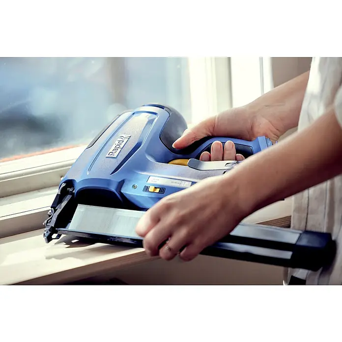 Rapid Power for All 18V Akku-Nagler BNX50 - 18 V, Ohne Akku, Länge Nagel: 20 mm - 50 mm - Nahaufnahme eines Rapid Elektrotackers in Blau, der von einer Person auf einer Fensterbank gehalten wird. Perfekt für schnelle und präzise Befestigungen.