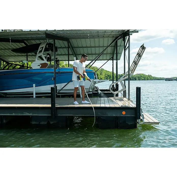 Ryobi ONE+ Akku-Hochdruckreiniger RY18PWX41A-0 - 18 V, Ohne Akku, Max. Druck: 41 bar - Ein Mann reinigt mit einem gelb-schwarzen Ryobi Akku-Hochdruckreiniger ein Bootsdeck am Wasser, unter einem Vordach, bei Tageslicht.