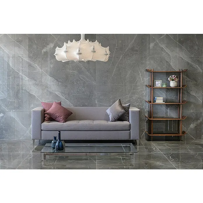 Feinsteinzeugfliese Amani Marble Light - 80 x 80 cm, Grau, Glänzend - Elegantes Wohnzimmer-Interieur mit einem stilvollen grauen Sofa, dekorativen Kissen und einem modernen Bücherregal, beleuchtet von einer Designerlampe.