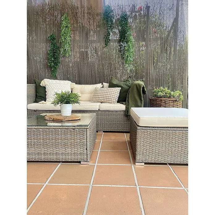 Nortene Ocultación de mimbre Fency Wick - L x Al: 3 x 1 m, Plástico, Antracita - Juego de muebles de exterior con sofá de ratán, mesa de centro con tapa de vidrio y otomana acolchada en un patio con baldosas. Plantas decorativas en la pared.