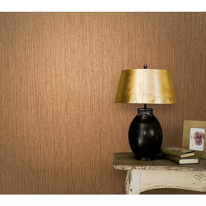 Marburg Modernista Vliestapete - Braun, Uni, 10,05 x 0,53 m - Warme braune Tapete mit feinem vertikalem Strukturmuster, hinter einer dunklen Lampe und einem Beistelltisch.